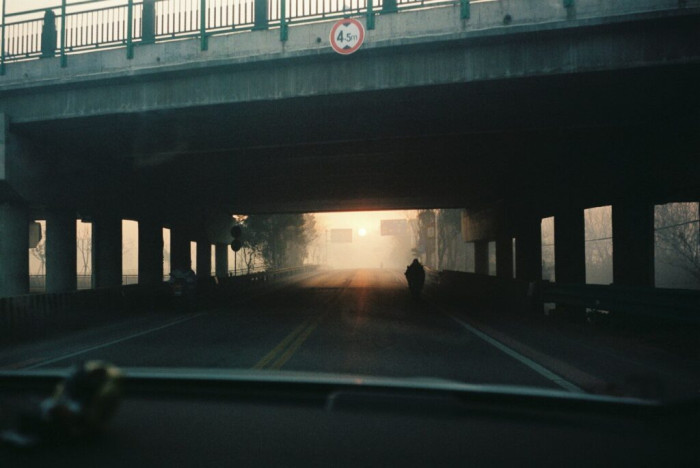 Hazy sunlight silhouettes a person under a dark overpass.