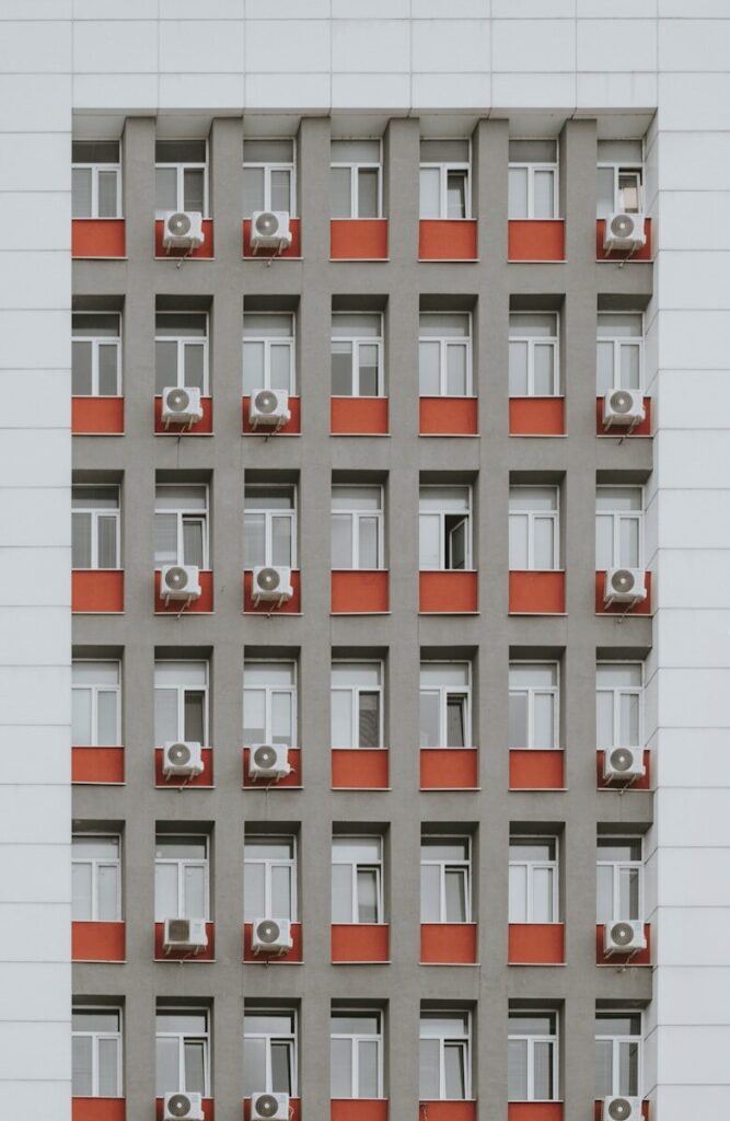 Grey building facade with red window accents and air conditioners