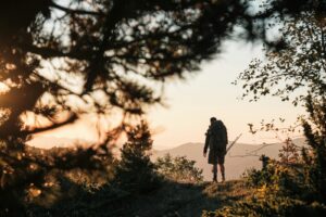 Hiker with backpack stands on a mountain at sunset.