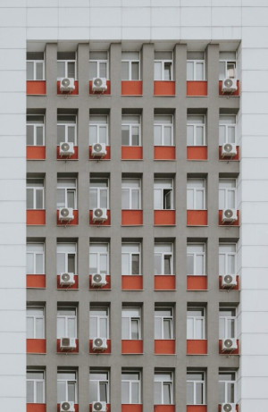 Grey building facade with red window accents and air conditioners