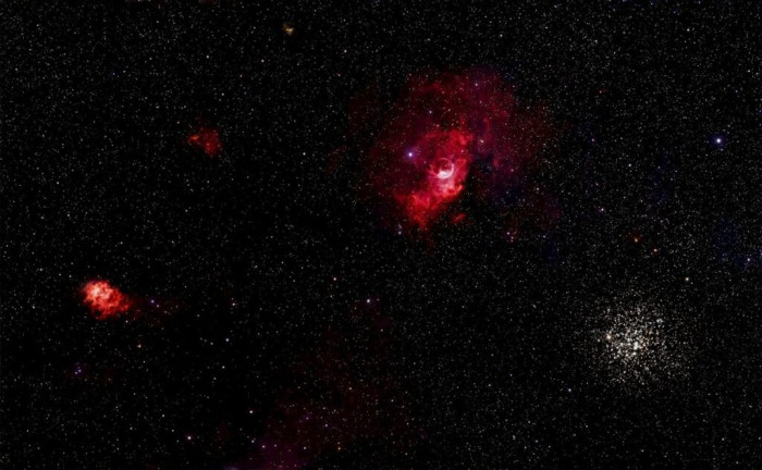 Dark space with red nebulas and a bright star cluster.