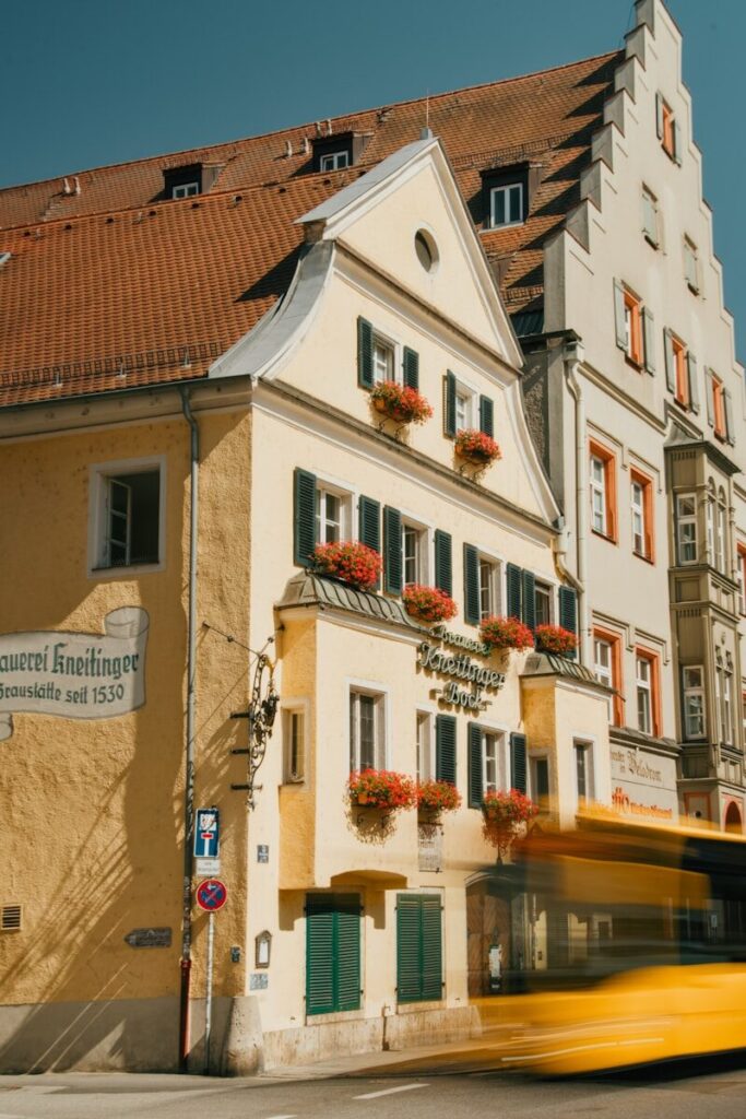 A yellow building with green shutters and red flowers in Regensburg, Germany.